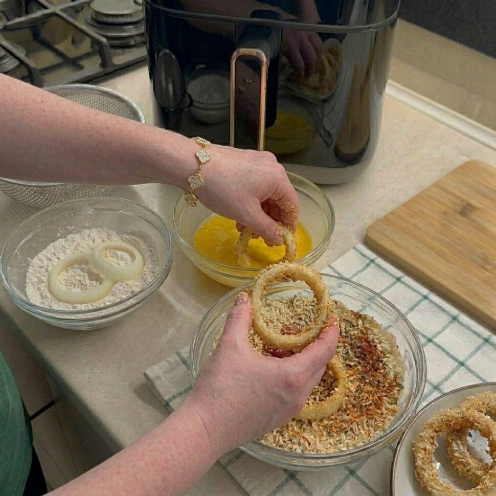 Bowls of flour egg wash and seasoned panko breadcrumbs set up for coating onion rings