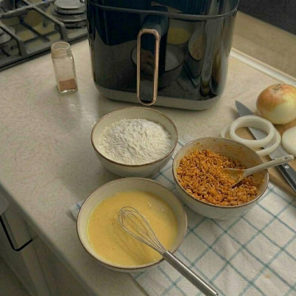 Bowls of flour egg wash and seasoned panko breadcrumbs set up for coating onion rings