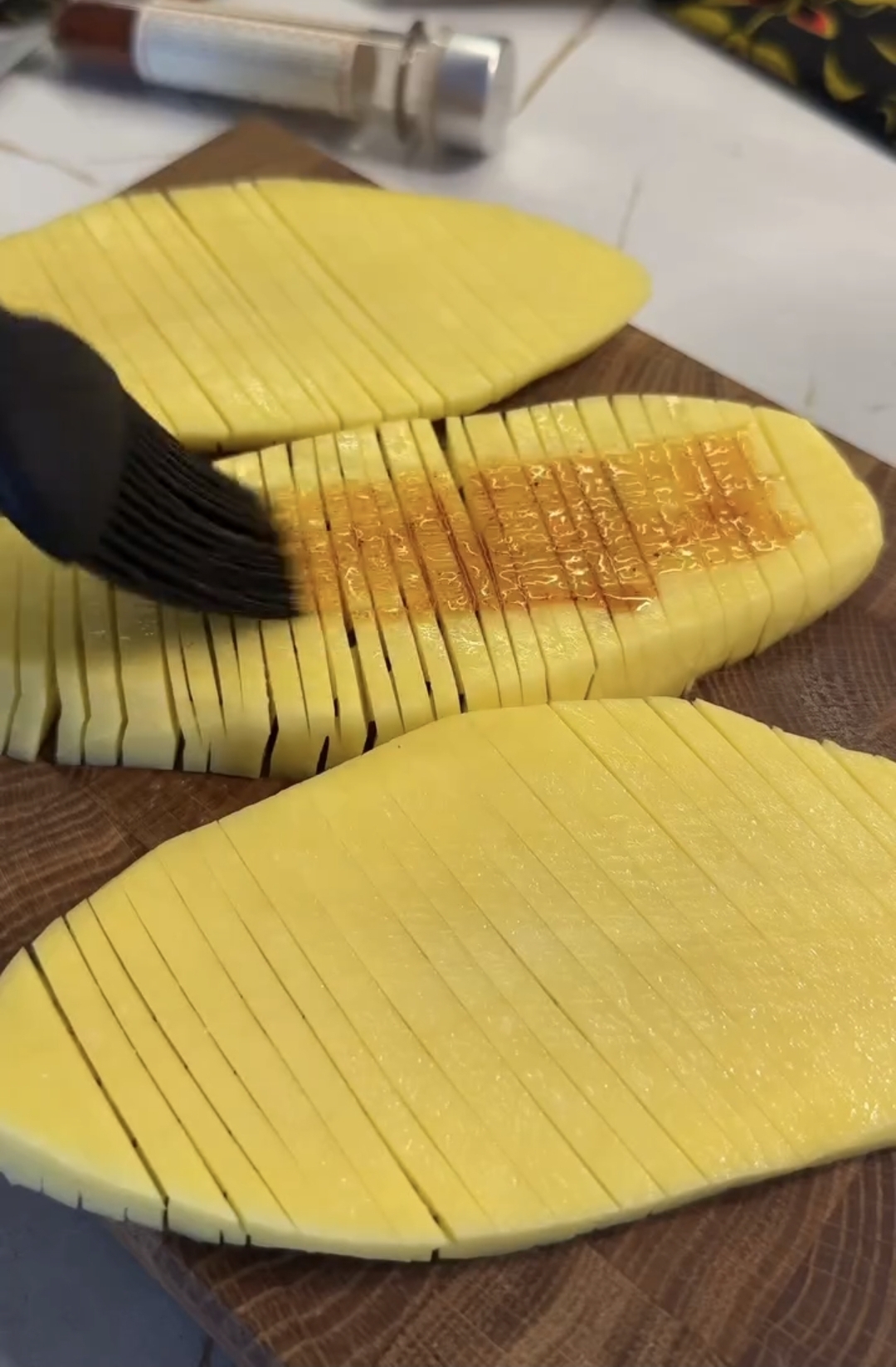 air fryer accordion potatoes being coated with a spiced oil mixture using a pastry brush